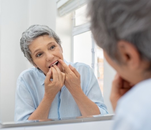 Older woman flossing her teeth in front of mirror