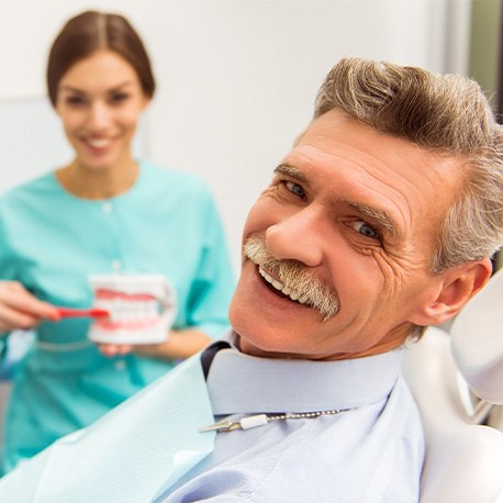 Man smiling at camera as dentist shows him how to brush dentures