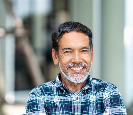 Man with gray beard in blue plaid shirt outside smiling